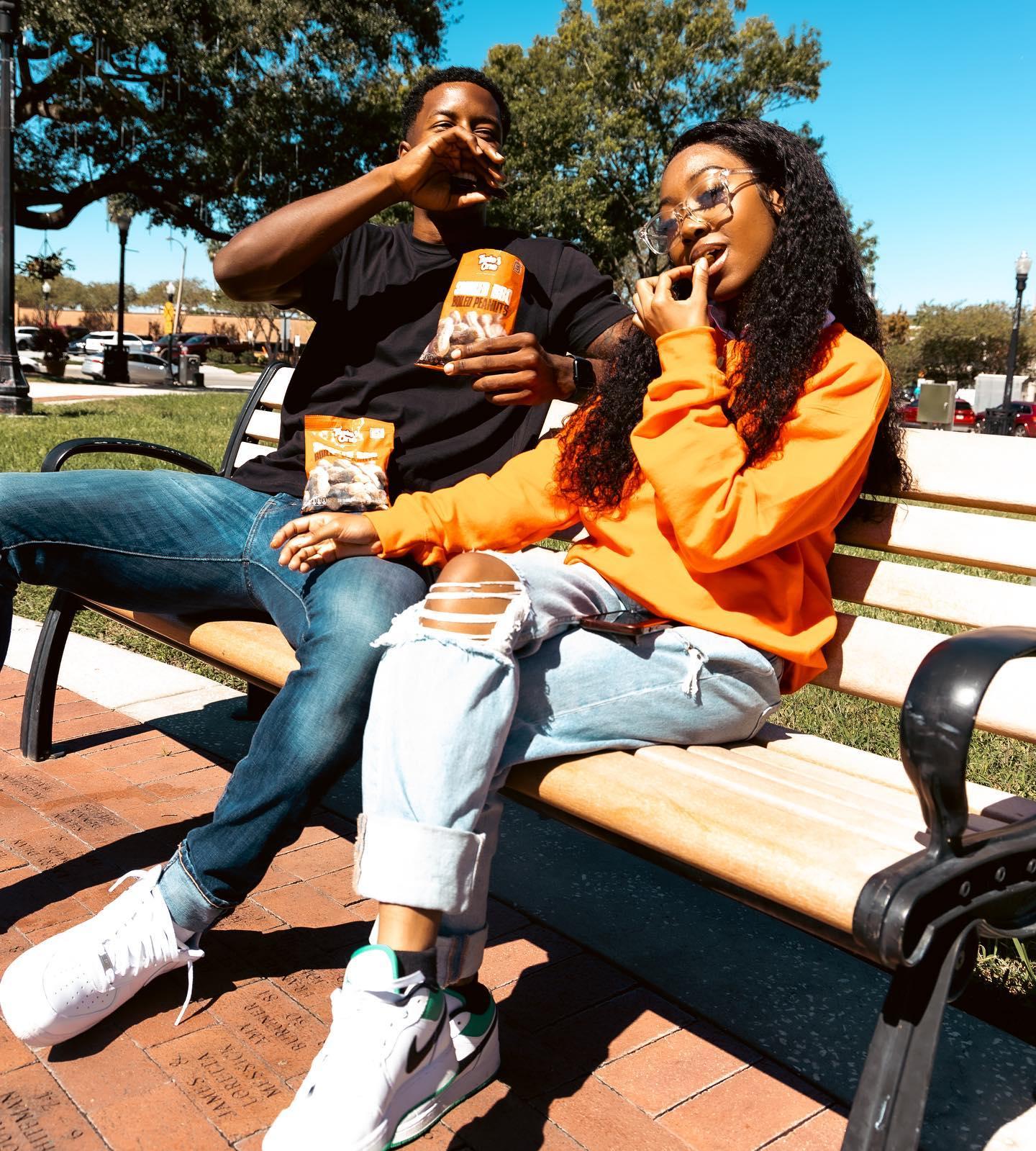 Two fans sharing a bag of Taste One boiled peanuts on a bench